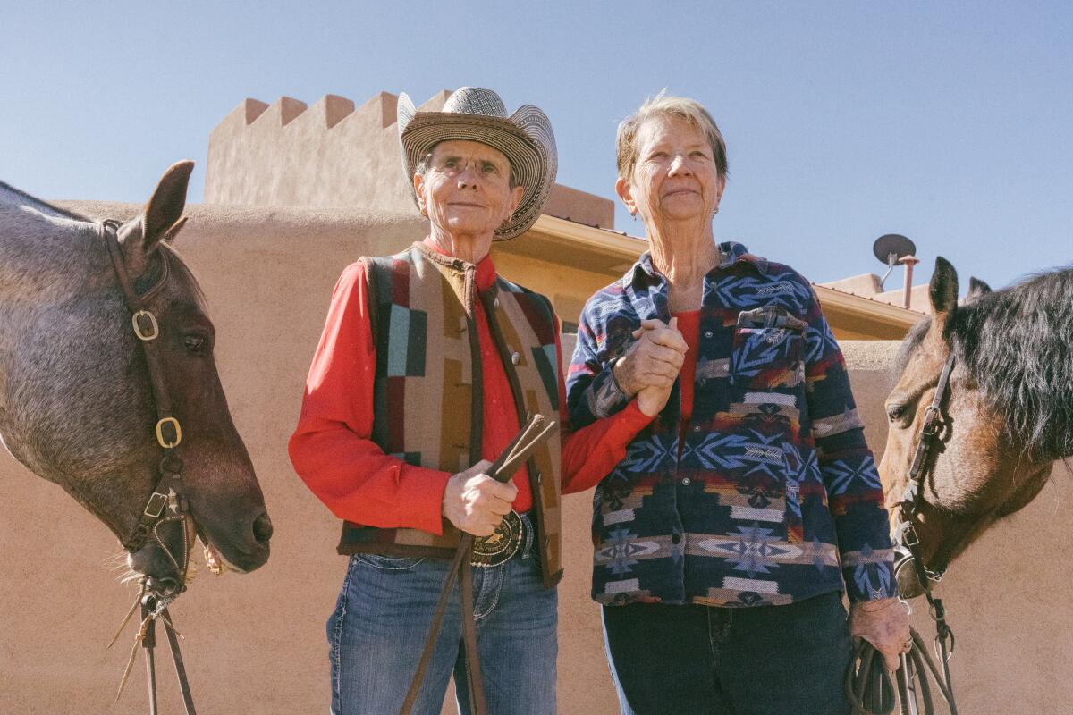 Terry Berg (left) and Helen Newton hold hands next to their horses at their home in Santa Fe, N.M.
