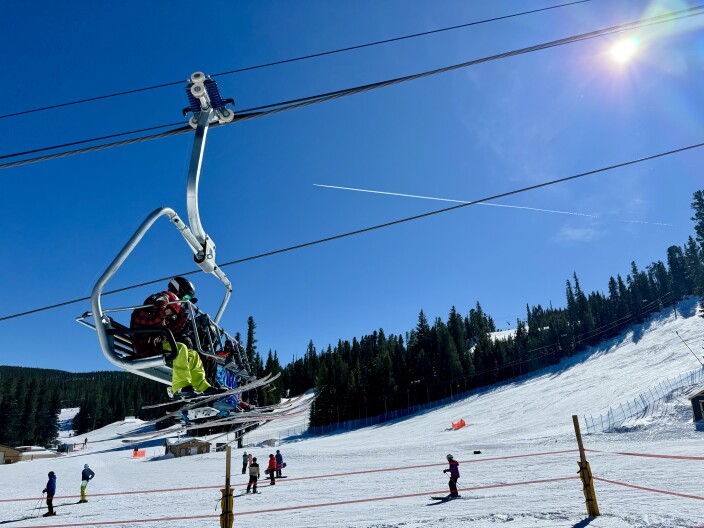 Skiers on a chairlift at Eldora Mountain on a sunny day