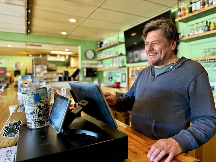 A worker stands behind a bar typing on a restaurant's Ipad checkout machine.