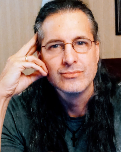 A man in glasses leans on his hand and looks directly into the camera