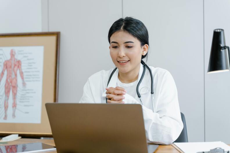 A female doctor sits behind a laptop.
