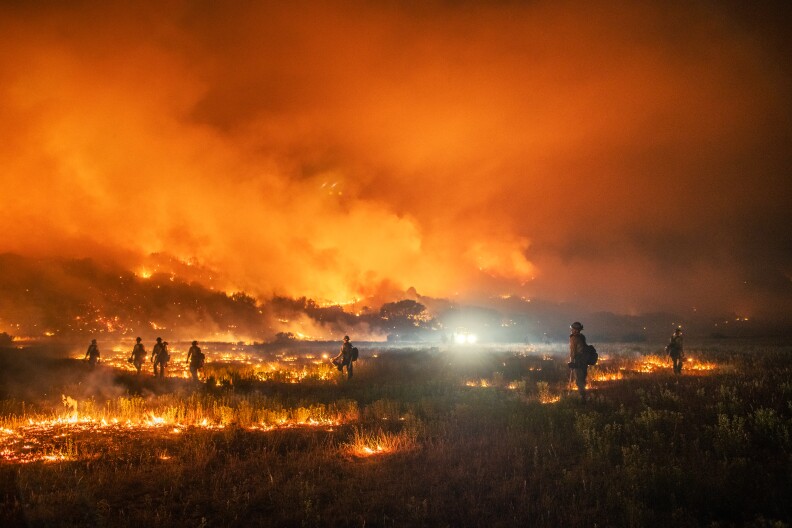 Flames are everywhere at night with some firefighters working.