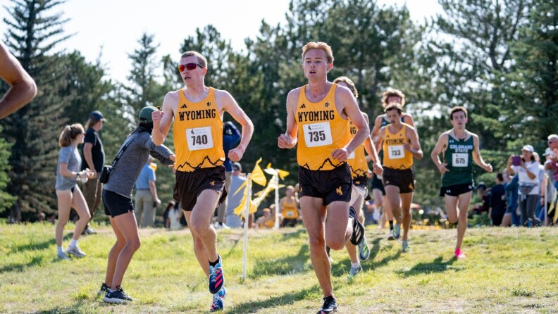 A group of men in uniforms run by. Two in Cowboys uniforms lead the pack.