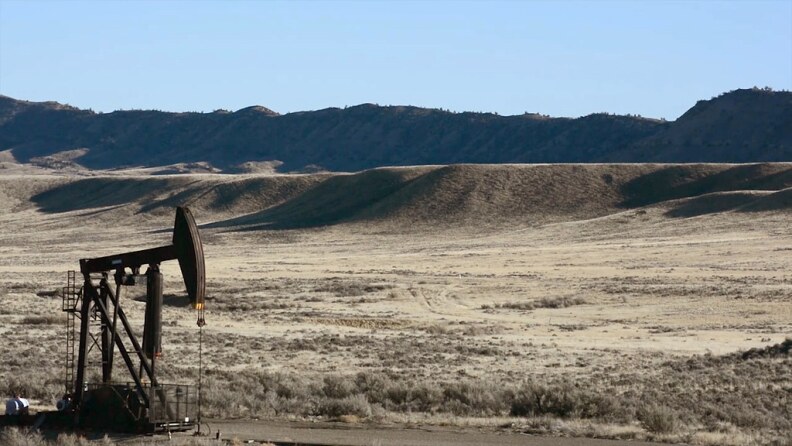 An oil well in front of golden grassy bluffs.