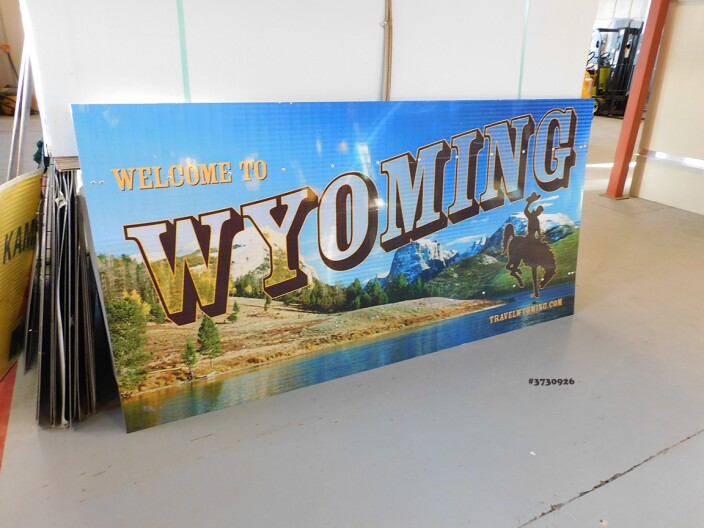 A sign that says “Welcome to Wyoming,” with a lake and mountains in the background.