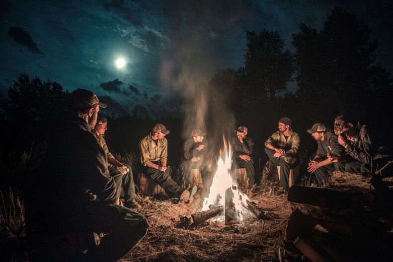 A group of people sit around a campfire at night
