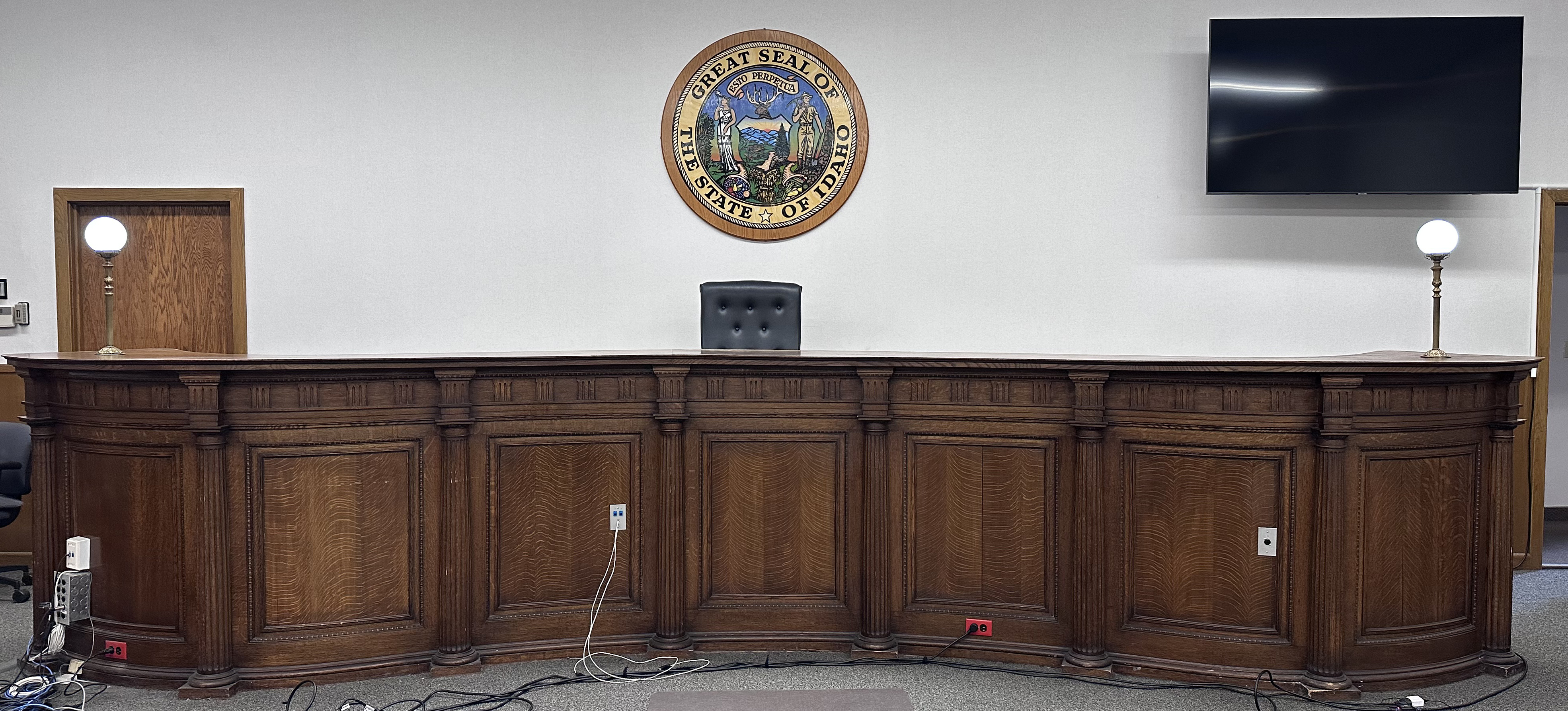 A wooden bench with a single black desk chair behind it and the great seal of the state of idaho