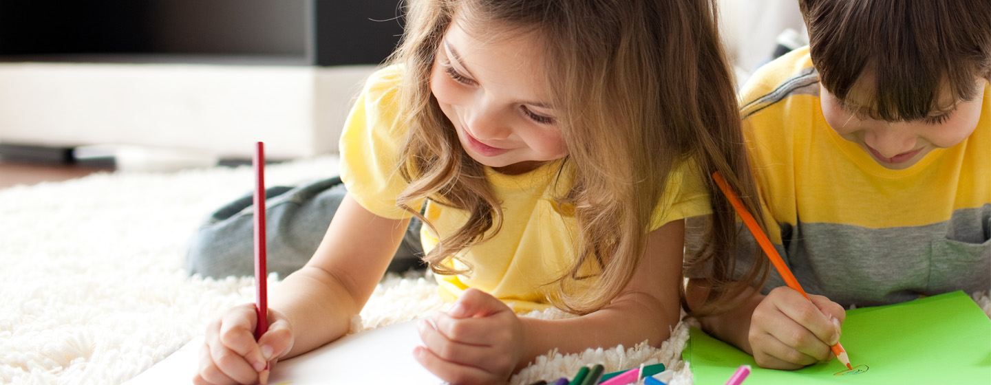 A young girl (left) and boy (right) laying on the floor coloring with colored pencils