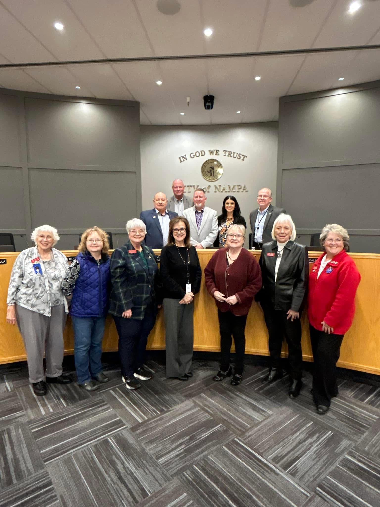 A group of people stand in a row, with grey walls and grey carpet