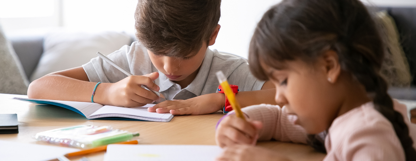 A young boy and girl writing in notebooks at a table.