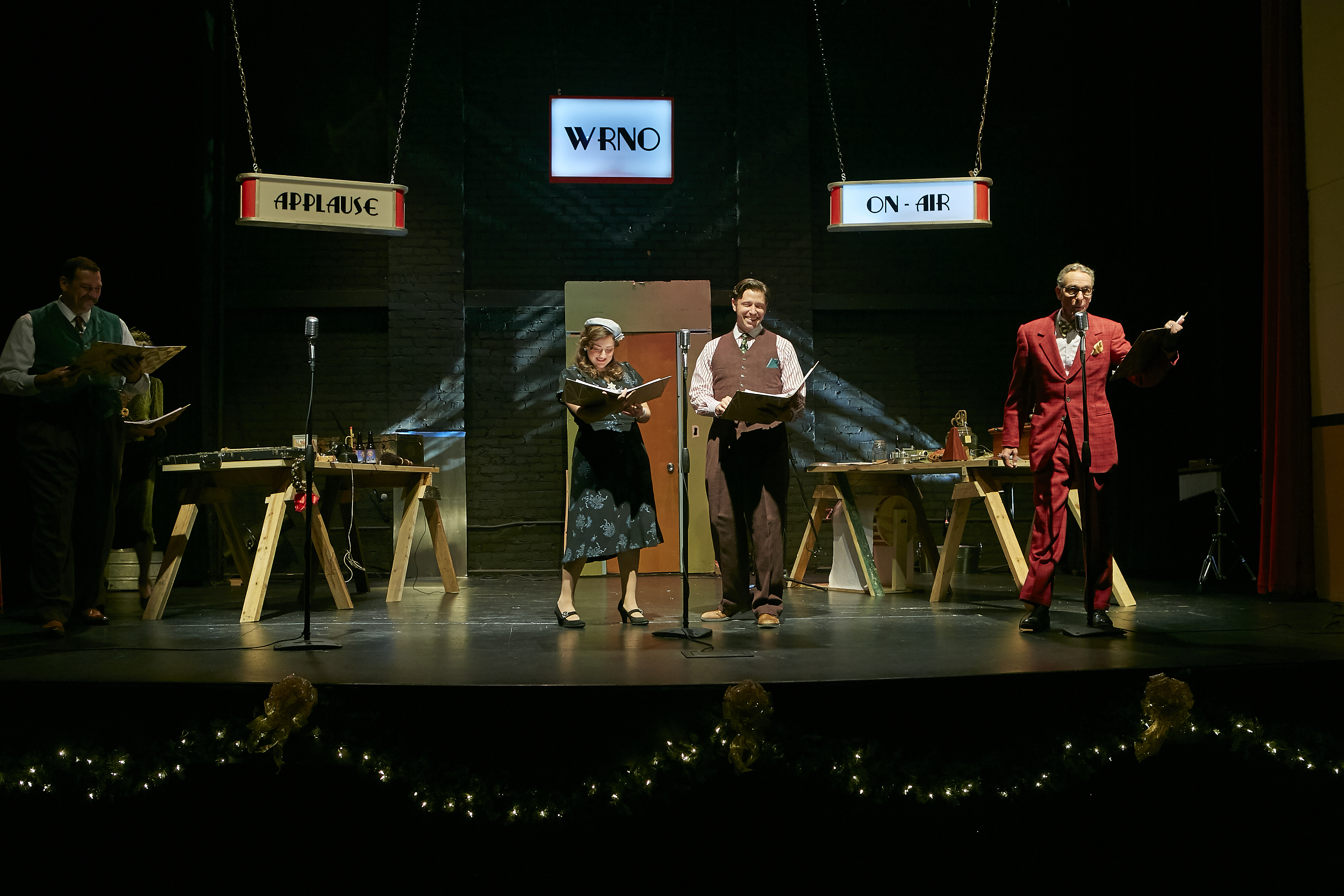 Four performers in period costumes act at vintage microphones on a radio-studio stage