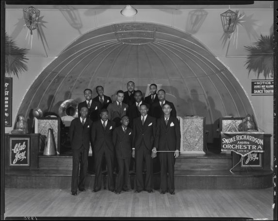 Smoke Richardson and his orchestra posed on a bandstand, with Richardson at the far right holding a baton