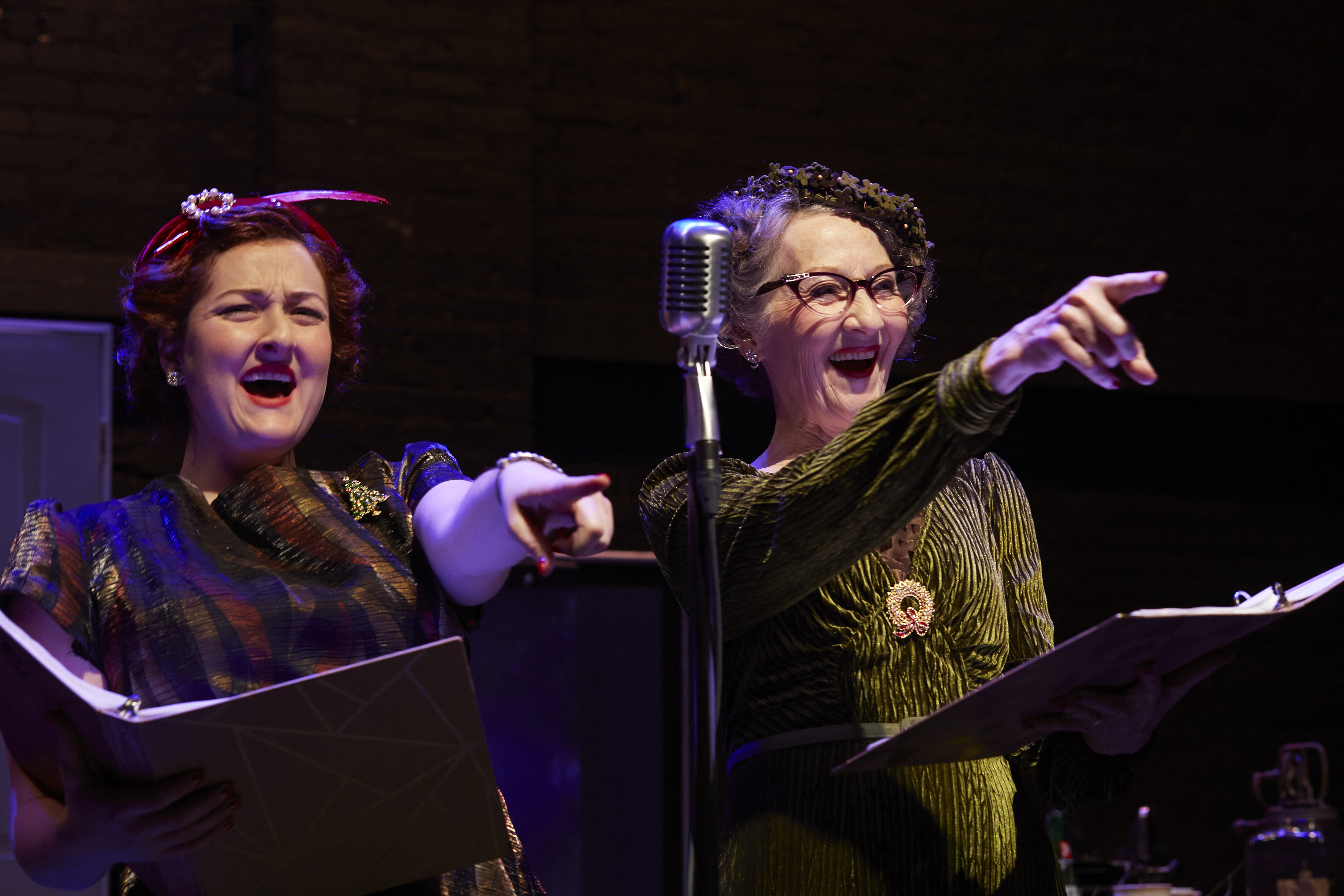 Two performers laugh and point toward the audience while acting at a vintage microphone