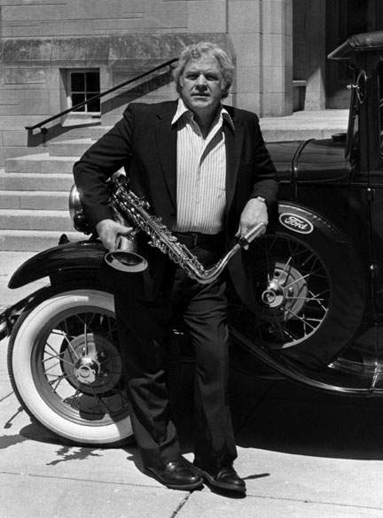 Musician Al Cobine in front of a vintage Ford vehicle holding a brass instrument