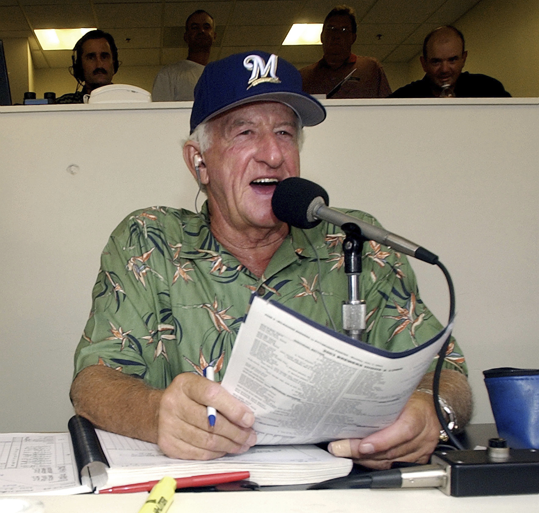 Bob Uecker wearing a Milwaukee Brewers cap while speaking into a radio microphone