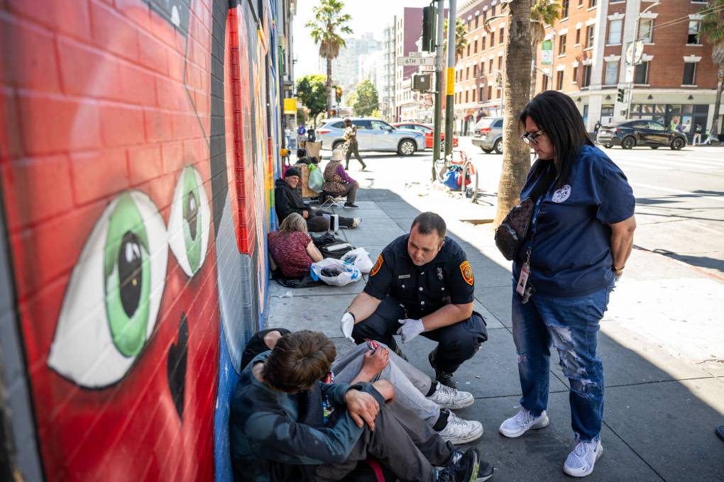 Paramedic Isaac James (left) and counselor Chantel Hernandez-Coleman, members of the Street Overdose Response Team, speak with 2 people sitting on the street in the South of Market neighborhood in San Francisco on Sept. 3, 2024. (Beth LaBerge/KQED)