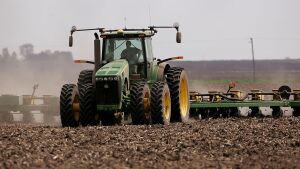 A green tractor that's planting corn moves across a brown dirt field in 2007 near Rochelle, Ill.
