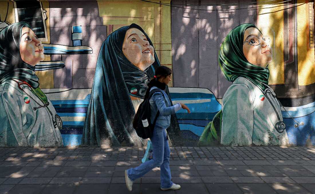 A woman walks past a wall mural along the roadside in Tehran on April 12, 2026.