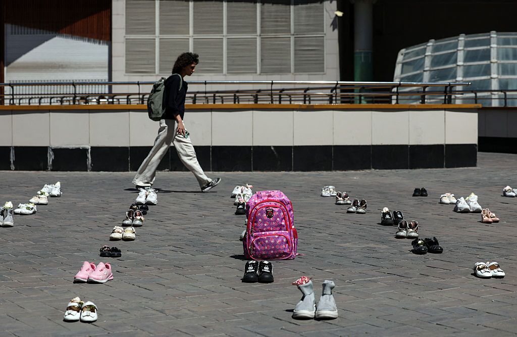 An Iranian woman walks past symbolic belongings laid on the ground at Valiasr Square in Tehran on April 24, 2026, in tribute to the schoolgirls in Minab killed in an airstrike.