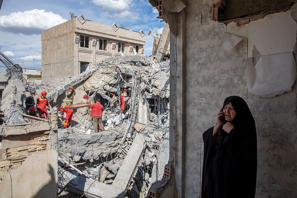 A woman speaks on the phone as emergency workers sift through rubble of a residential building that was hit in an airstrike in the early hours of March 27, 2026 in Tehran, Iran. (Getty Images Europe)