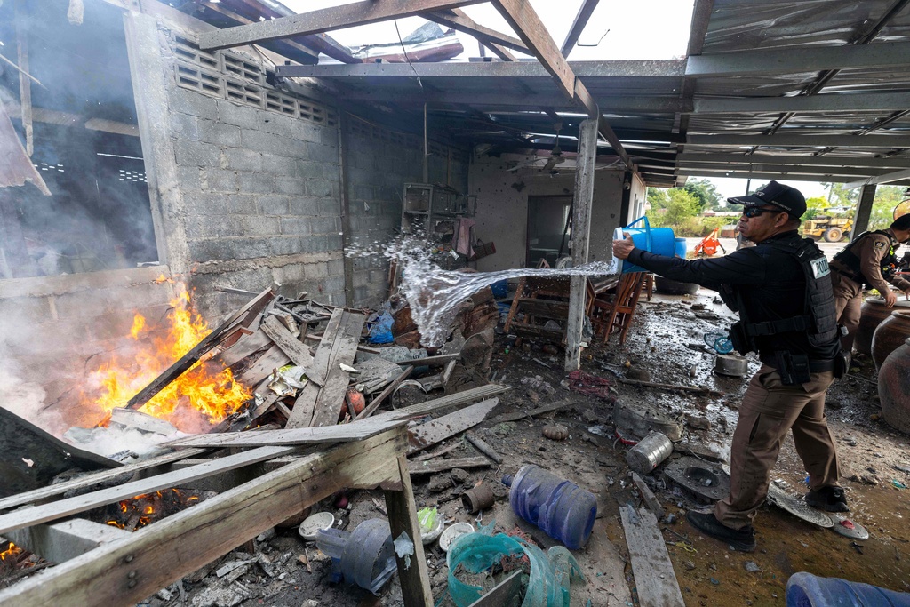 A Thai police officer splashes water to control fire Thursday at a house in Surin Province, which Thai local security forces say was damaged by a Cambodian artillery strike.