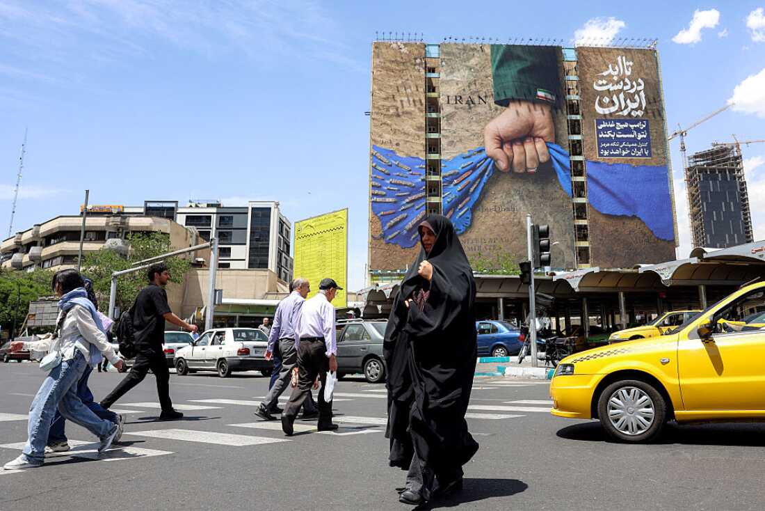 A woman crosses a street near a billboard on a building depicting the Strait of Hormuz with a caption in Persian reading "Forever in Iran's Hand," at Vanak Square in Tehran, Iran, on Wednesday.