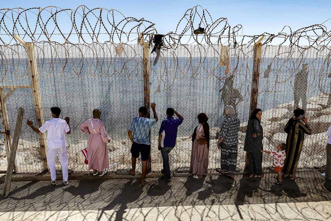 Relatives and friends wait by a fence topped with barbed-wire for the return of people who had previously crossed into Spain's North African enclave of Ceuta, at Morocca's Bab Sebta border crossing on the outskirts of Fnideq on August 2, 2026.