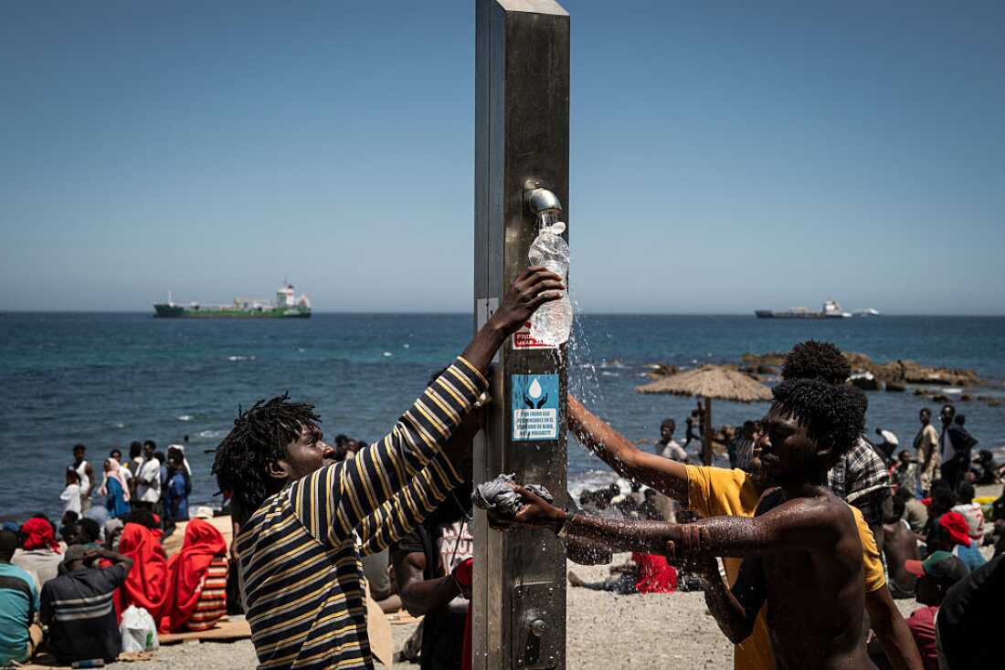 Migrants fill bottles with water on the beach next to the CETI (Centros de Estancia Temporal de Inmigrantes) on August 2, 2026 in Ceuta, Spain.