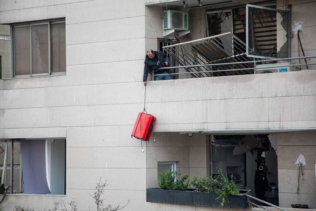 A man lowers a suitcase from the balcony of a building damaged by a US-Israeli strike on a commercial district on March 29, 2026 in Tehran, Iran.