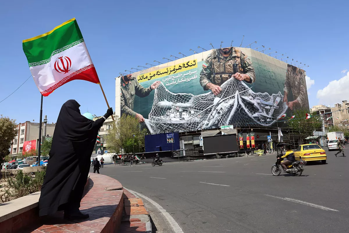 TOPSHOT - A woman holds Iran's national flag while standing near a billboard with a sentence reading 'The Strait of Hormuz remains closed' at the Enqelab Square in Tehran, on April 5, 2026.