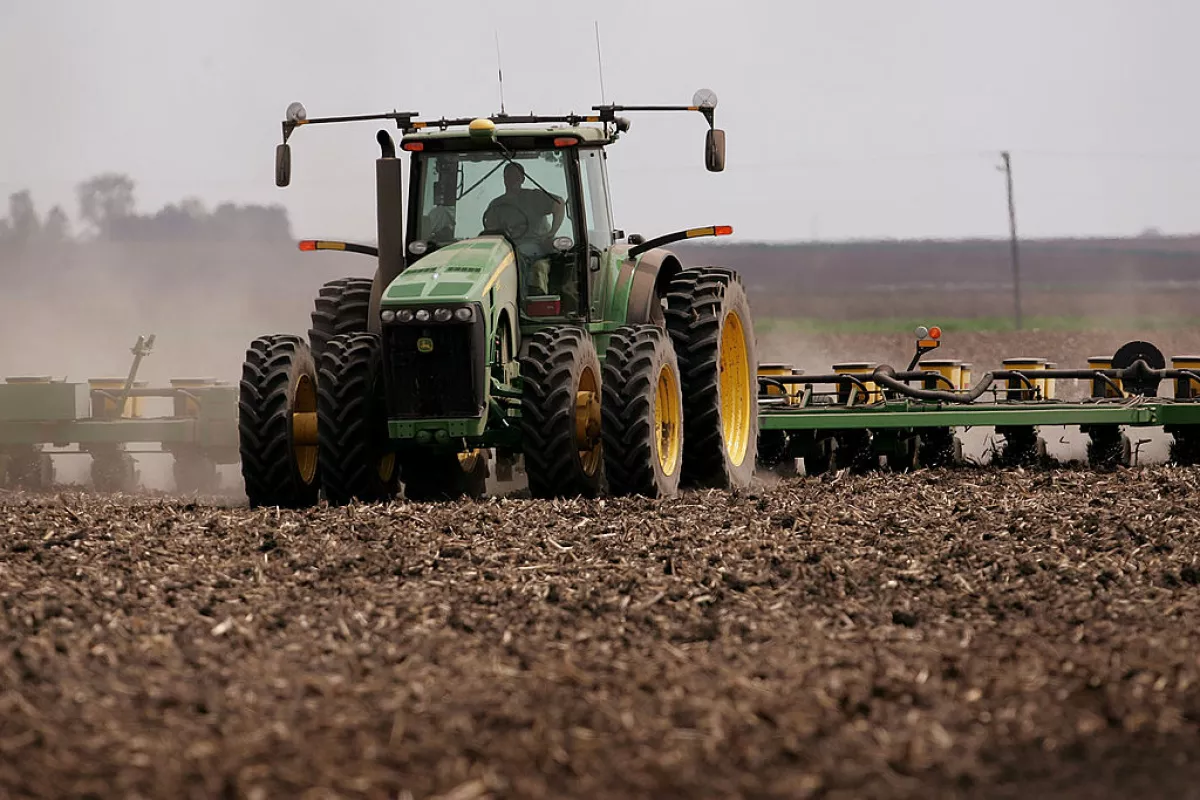 A green tractor that's planting corn moves across a brown dirt field in 2007 near Rochelle, Ill.