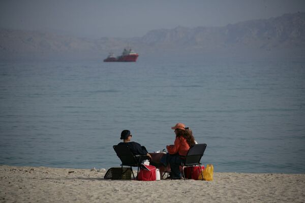 People sit on the beach with ships in the distance on April 24, 2026 in Kish Island, Iran.
