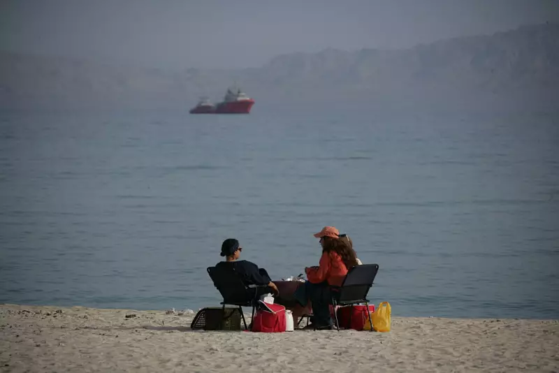People sit on the beach with ships in the distance on April 24, 2026 in Kish Island, Iran.