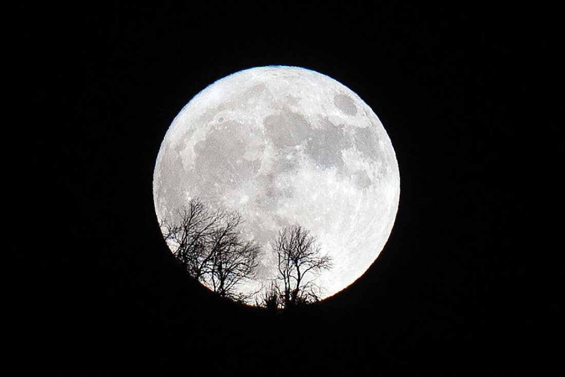 A full supermoon rises behind a mountain.