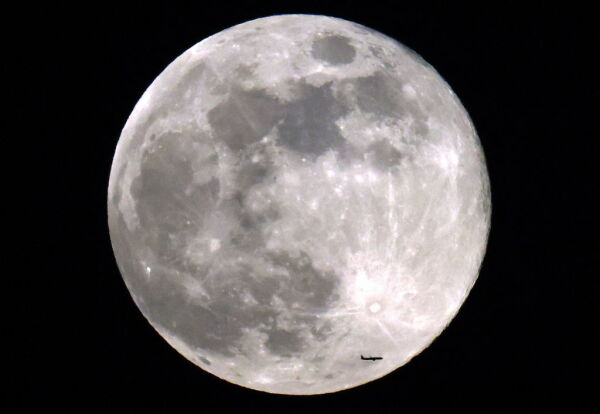 A commercial airliner flies before the rising Beaver full moon above Kuwait City on Nov. 27, 2023.