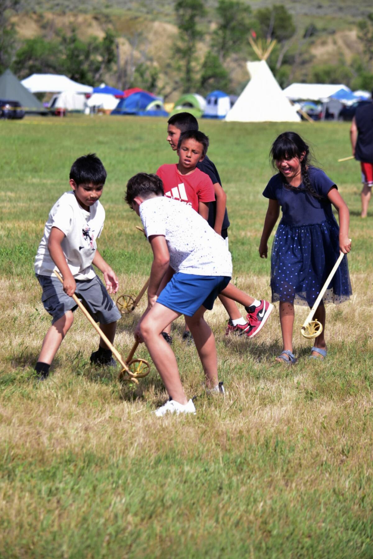 A group of children from different tribal nations play lacrosse together using traditional equipment.