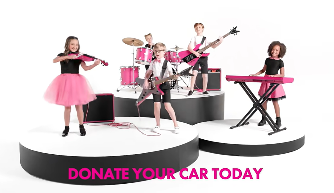 A still from a Kars4Kids TV commercial, showing children playing pink instruments and the words "donate your car today."