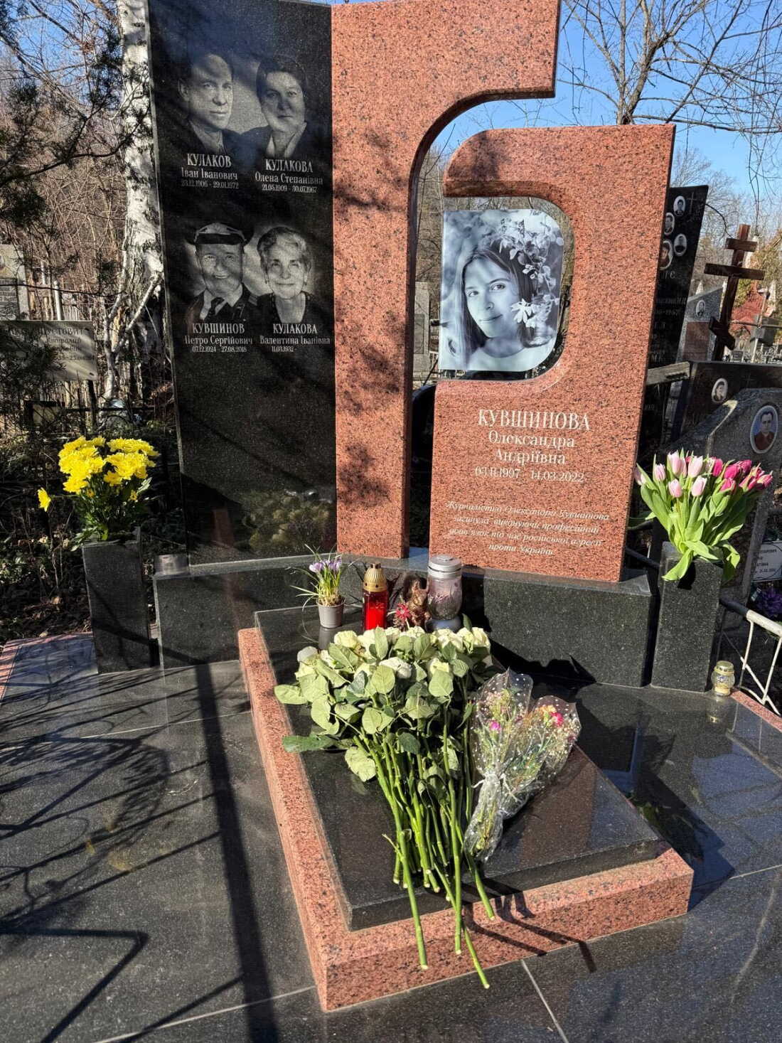 Flowers and candles rest on the headstone for Oleksandra Kuvshynova. The headstone includes a black-and-white photo of her.