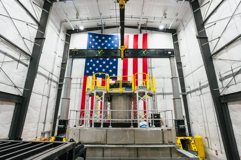 Aalo Atomics' Aalo-X Critical Test Reactor stands inside the company's facility in Idaho Falls, Idaho. A large American flag hangs vertically on the facility's back wall.