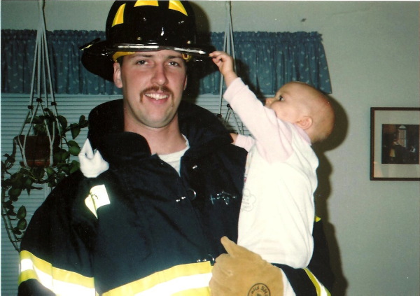 A family photo of Doug Miller in his firefighter uniform carrying Elizabeth, when she was a baby.