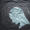 Negative emotion image. Person head shaped paper on black torn paper background.