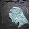 Negative emotion image. Person head shaped paper on black torn paper background.