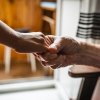 A closeup photo of two hands demonstrates an older man clasping the hand of a person who is offering a helping hand.