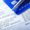 A hospital bill for $36,000 with a line item of various charges is photographed with a very shallow depth of field. A credit card and a ballpoint pen rest out of focus in the background.