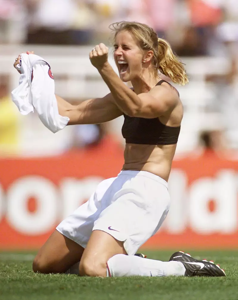 Brandi Chastain celebrates after kicking the winning penalty kick at the 1999 women's World Cup final on July 10, 1999. She is kneeling on the grass and has raised her arms upward.