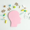 A pink head with a puzzle piece on it. There are many pills scattered around the head. Some of the pills are yellow and some are green
