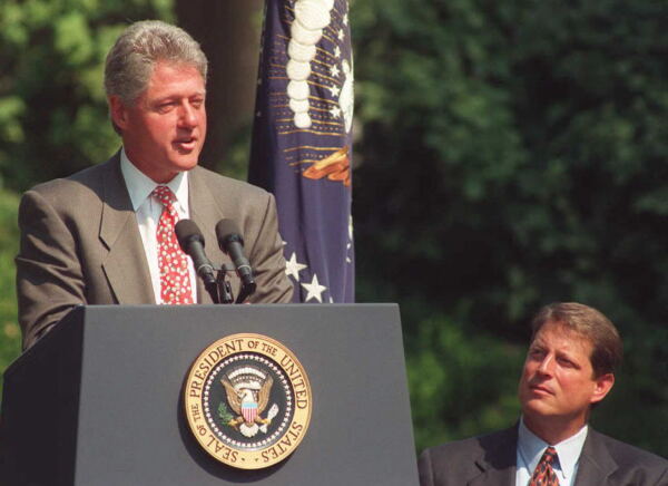 In this 1995 photo, President Bill Clinton is standing outdoors behind a lectern with microphones attached to it as he discusses his Reinventing Government initiative. Vice President Al Gore is on the right side of the photo.
