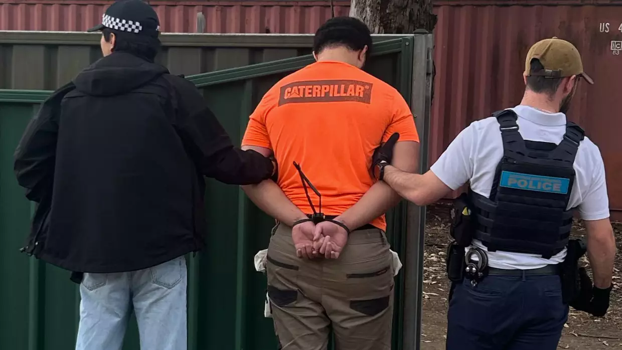 In this photo provided by the Australian Federal Police, a man, center, is arrested by police in Londonderry in western Sydney, Friday, June 19, 2026.