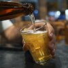A hand holds a glass while a bottle of beer is poured into the glass.