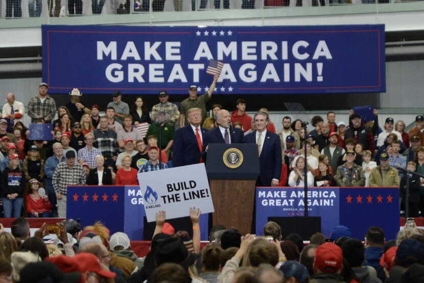 Commerce Secretary Howard Lutnick talks about the proposed trans-Alaska natural gas pipeline in front of President Donald Trump, left, and Interior Secretary Doug Burgum on Tuesday, Oct. 13, 2026, in Wasilla. In the foreground, a rally attendee holds up a sign urging construction of the pipeline.